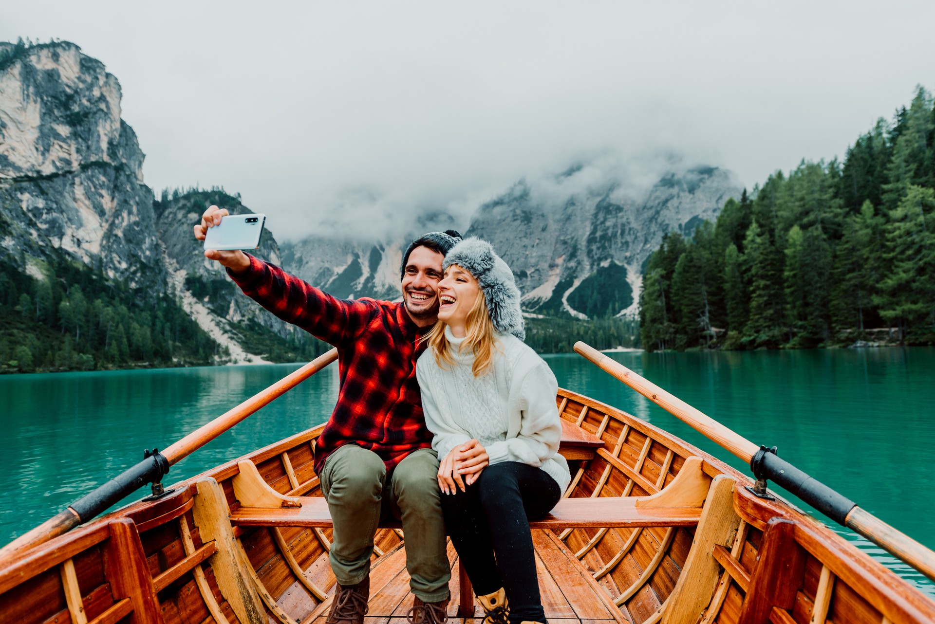 Romantic couple of adults in love taking a selfie on a boat visiting an alpine lake at Braies Italy at autumn fall. Couple, wanderlust and travel concept. Cold colours.